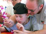 father helping young boy learn to string an orchid on a long lei needle 